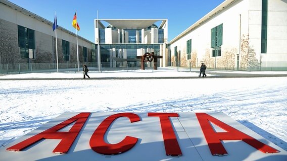Vier rote ACTA-Buchstaben liegen vor dem Bundeskanzleramt in Berlin auf einer Holzfläche im Schnee. © dpa Foto: Rainer Jensen