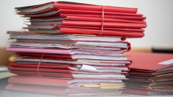 Ein Haufen roter Aktenmappen stapeln sich auf einem Schreibtisch. © dpa - picture alliance Foto: Monika Skolimowska