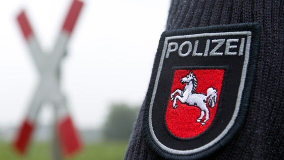Ein Polizeiwappen auf einem Ärmel ist an einem unbeschrankten Bahnübergang mit Andreaskreuz zu sehen. Ein Polizeiwappen auf einem Ärmel ist an einem unbeschrankten Bahnübergang mit Andreaskreuz zu sehen. © picture alliance / dpa | Friso Gentsch Foto: Friso Gentsch
