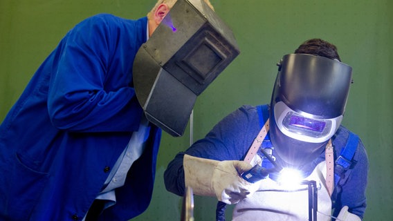 Ein Auszubildender setzt eine Schweißnaht an ein Metallteil, während ein Berufsschullehrer zuschaut. © dpa Bildfunk Foto: Daniel Bockwoldt