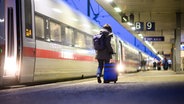 Eine Frau läuft in den Morgenstunden, der Morgen dämmert, mit einem Rollkoffer über einen Bahnsteig im Hauptbahnhof Hannover an einem stehenden ICE entlang. © picture alliance/dpa Foto: Julian Stratenschulte