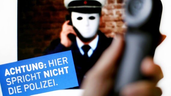 Ein Telefonhörer ist vor einem Plakat der Polizei NRW mit der Aufschrift «Achtung: Hier spricht nicht die Polizei» zu sehen.  Foto: Martin Gerten