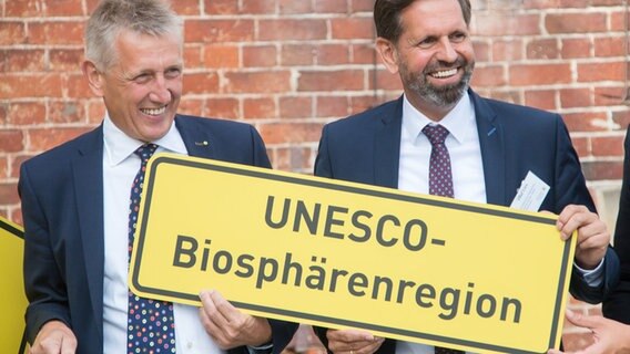 Der Leiter der Nationalparkverwaltung, Peter Südbeck und Umweltminister Olaf Lies (SPD  halten ein Ortsschild mit dem Titel «Unesco-Biosphärenregion». © dpa-Bildfunk Foto: Lennart Stock