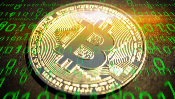 Eine Münze mit dem Bitcoin-Logo mit einem binären Zahlencode (grünes Licht) überzogen. © picture alliance/chromorange Foto: Christian Ohde