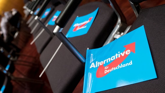 Auf Stühlen bei einer Wahlkampfveranstaltung der AfD liegen Fähnchen mit dem Parteilogo. © dpa - Bildfunk Foto: Peter Steffen