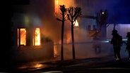 Feueerwehrleute stehen vor einem brennenden Gebäude. © NonstopNews 