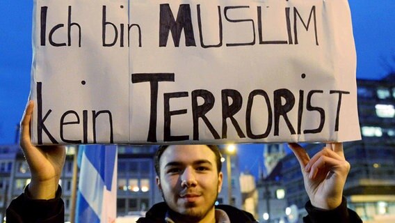 Ein junger Mann hält am Rande einer Demonstration ein Schild mit der Aufschrift "Ich bin Muslim kein Terrorist" in die Luft. © NDR Foto: Marco Schulze