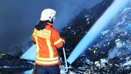 Ein einer Lagerhalle in Braunschweig wird ein brennender Müllhaufen von einem Feuerwehrmann gelöscht. © TeleNewsNetwork 