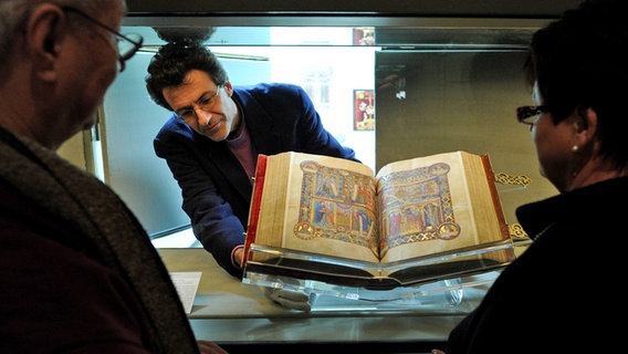 Ein Mann richtet das aufgeblätterte Evangeliar Heinrichs des Löwen in einem Schaukasten ein. © dpa-Bildfunk Foto: Jochen Lübke