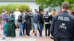 Ein Polizist steht im Erstaufnahmelager für Flüchtlinge in Friedland vor wartenden Flüchtlingen. © dpa-Bildfunk Foto: Swen Pförtner