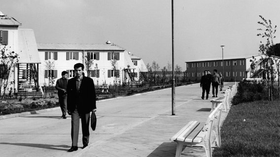 Arbeiter gehen eine Straße entlang © Institut für Zeitgeschichte und Stadtpräsentation, Stadt Wolfsburg Foto: Willi Luther