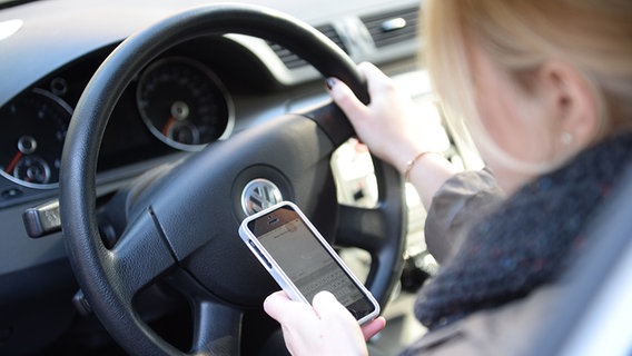 Eine Frau sitzt im Auto am Steuer und liest Nachrichten auf ihrem Smartphone. © dpa Foto: Monika Skolimowska