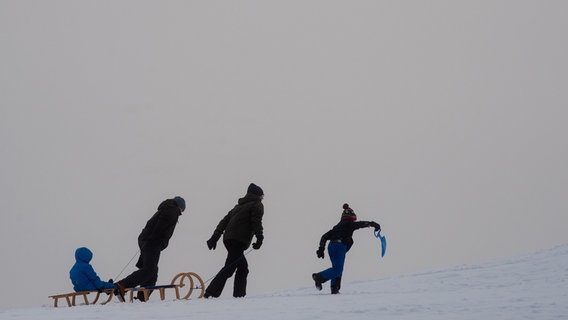 Wintersportler gehen mit ihren Schlitten einen Rodelhang am Sonnenberg im Harz hinauf. © dpa-Bildfunk Foto: Swen Pförtner