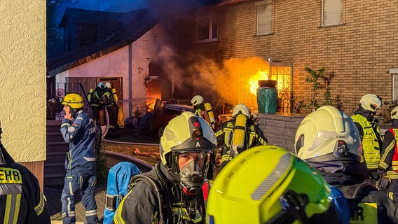 Mehrere Feuerwehrleute stehen vor einem brennenden Haus, sie tragen Atemschutzgeräte. © Kreisfeuerwehr Northeim Foto: Kreisfeuerwehr Northeim