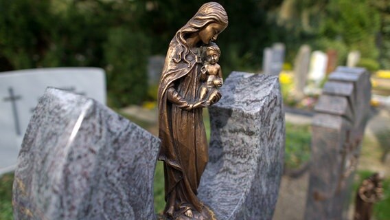 Eine kleine Madonnenstatue auf einem Grabstein auf einem Friedhof. © dpa Foto: Uwe Anspach