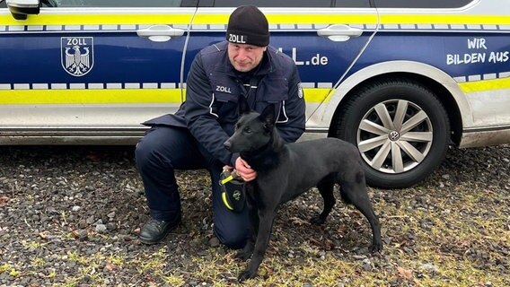 Ein Hundeführer der Polizei posiert mit seinem Hund vor einem Dienstwagen. © Hauptzollamt Braunschweig 