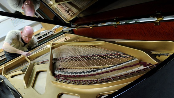 Ein Mitarbeiter von Grotrian-Steinweg reguliert eine Klaviermechanik am geöffneten Instrument. © dpa Foto: Caroline Seidel