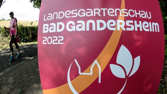 Der Schriftzug "Landesgartenschau Bad Gandersheim 2022" ist auf einem Plakat beben einer Sportlerinn auf dem Gelände der Landesgartenschau zu sehen. © dpa Foto: Swen Pförtner