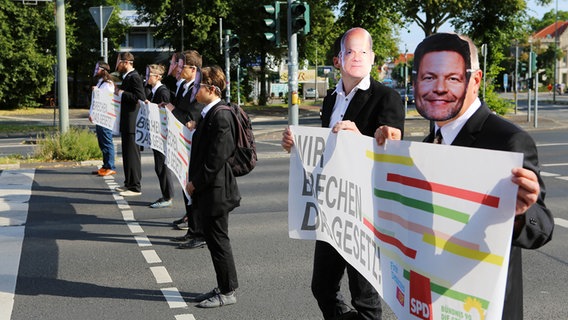 Klimaaktivisten der Gruppe "Letzte Generation" stehen mit Masken von Bundeskanzler Scholz (l) und Wirtschaftsminister Habeck bei einer Blockade auf einer Kreuzung in Göttingen. © dpa-Bildfunk Foto: Stefan Rampfel