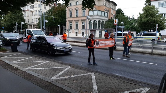 Aktivisten der Gruppe "Letzte Generation" protestieren auf einer Straße. Dahinter staut sich der Verkehr. © Letzte Generation Braunschweig Foto: Letzte Generation Braunschweig