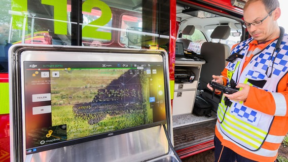 Ein Drohnenpilot der Feuerwehr neben einem Monitor und Feuerwehrwagen. © Julian Stratenschulte/dpa Foto: Julian Stratenschulte
