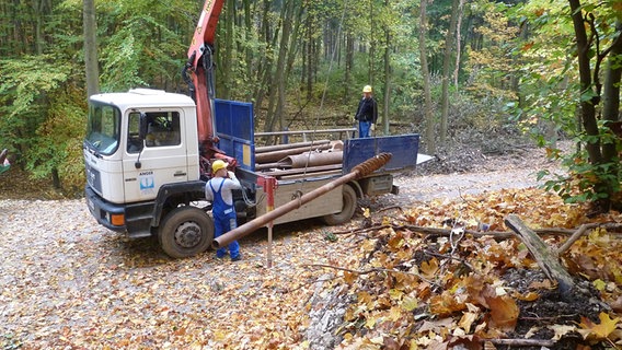 In der Totalen sind zwei Männer zu sehen, die an einer Bohrung auf einem Lkw im Wald arbeiten. © NDR.de Foto: Peter Jagla