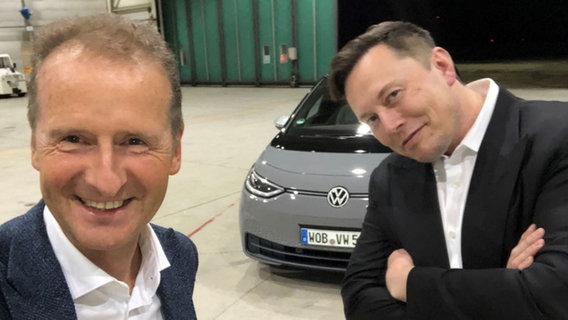 Herbert Diess, Vorstandsvorsitzender der Volkswagen AG, fotografiert sich zusammen mit Elon Musk, Tesla-Chef, in einem Hangar des Braunschweiger Flughafens. © Volkswagen AG/dpa 