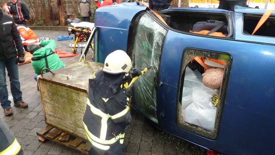 Ein Feuerwehrmann sägt die Frontscheibe eines auf der Seite liegenden Autos auf. © NDR.de Foto: Jürgen Jenauer