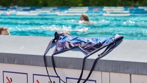 Ein Badeanzug liegt auf einer Mauer im Prinzenbad, dahinter schwimmen Menschen im Becken ihre Bahnen. © picture alliance/dpa/Annette Riedl Foto: Annette Riedl