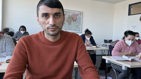 Das Bild zeigt Ortskraft Ahmad in einer Gruppe von Menschen sitzen. © NDR 