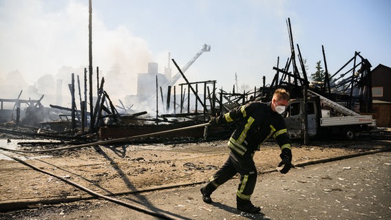 Ein Feuerwehrmann zieht einen Schlauch hinter sich her. Dahinter: eine abgebrannte Fläche. © Julian Stratenschulte/dpa Foto: Julian Stratenschulte