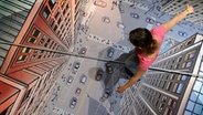 Eine Frau balanciert auf einem Seil über eine am Boden aufgemalte Stadt. © dpa-Bildfunk Foto: Julian Stratenschulte