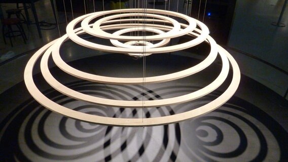 Neun konzentrische Kreise die an Fäden hängen, simulieren eine sich ausbreitende Kreiswelle Round Wave. Hierbei handelt es sich um ein Kunstwerk von Reuben Margolin, das im Wolfsburger Wissenschaftsmuseum Phæno gezeigt wird. © NDR Foto: Imke Caselli