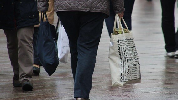Eine Frau hält zwei voll bepackte Jutebeutel in den Händen, während sie durch eine Einkaufspassage geht. © NDR Foto: Marco Schulze