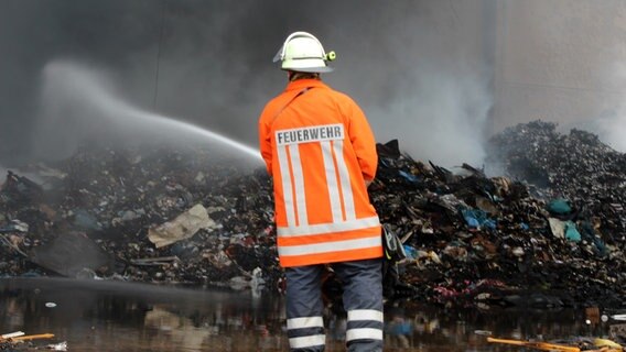 Ein Feuerwehrmann löscht einen brennenden Müllberg. © NDR Foto: Wolf-Hendrik Müllenberg