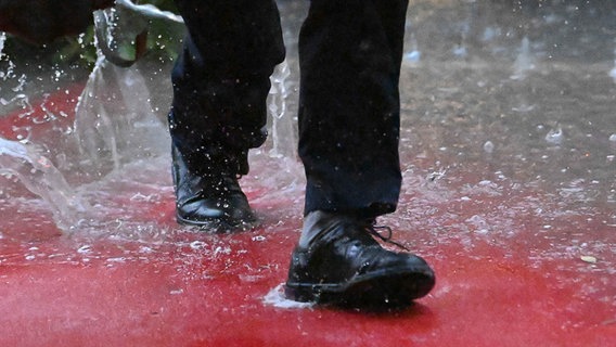 Ein Mann geht durch eine Regenpfütze. © picture alliance / dpa | Swen Pförtner Foto: Swen Pförtner