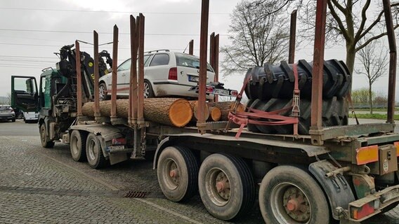 Ein weißer Pkw befindet sich auf einem mit Holzstämmen beladenen Lkw-Anhänger. © Polizeiinspektion Göttingen 