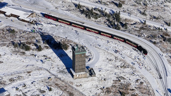 Eine Luftaufnahme zeigt eine feine Schneedecke über dem Brocken, auf dem eine Eisenbahn fährt. © Thomas Meder Foto: Thomas Meder