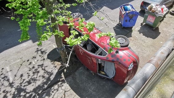 Ein auf der Seite liegendes Schrottauto im Hof eines heruntergekommenen Wohnblocks in Göttingen. © NDR Foto: Wieland Gabcke