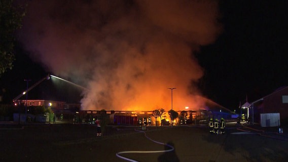 Auf dem Foto ist es Nacht, im Hintergrund ist ein großer Feuerschein zu sehen. Vorne stehen mehrere Einsatzkräfte der Feuerwehr und löschen, ein Schlauch liegt auf dem Boden. Auf dem Foto ist es Nacht, im Hintergrund ist ein großer Feuerschein zu sehen. Vorne stehen mehrere Einsatzkräfte der Feuerwehr und löschen, ein Schlauch liegt auf dem Boden. © Hannover Reporter