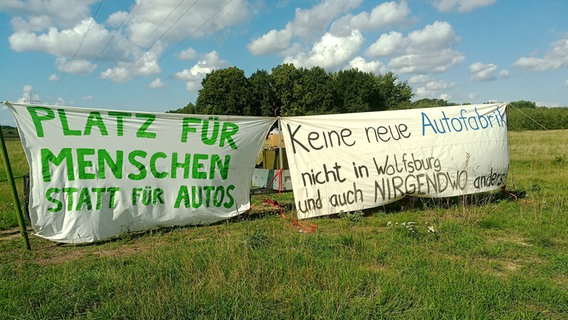 Transparente mit der Aufschrift "Platz für Menschen, statt für Autos" und "Keine neue Autofabrik" stehen auf einer Wiese. © NDR Foto: Frank Ihben