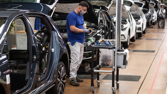 Ein VW-Mitarbeiter mit einem Mund- und Nasenschutz steht in der Produktion neben einem Auto im Werk in Wolfsburg. © picture alliance/dpa Foto: Swen Pförtner