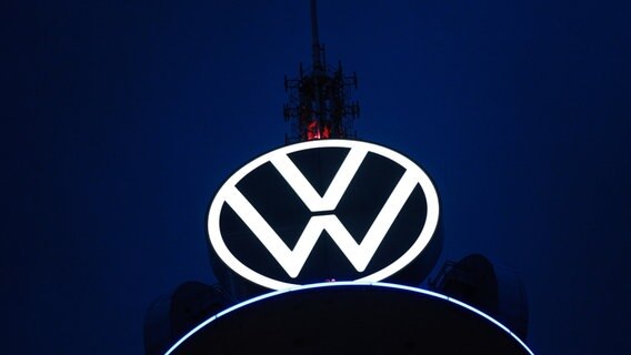 Das Volkswagen Logo leuchtet auf dem VW-Tower vor dunklem Himmel. © dpa Foto: Ole Spata