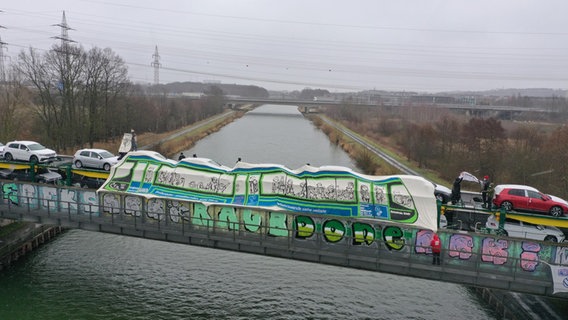 Klimaaktivsten haben einen Autozug mit Fahrzeugen von Volkswagen auf einer Brücke gekapert und mit Transparenten zu einer Straßenbahn verkleidet. © verkehrswendestadt.de 