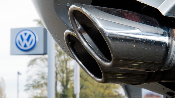 Der Auspuff eines Fahrzeuges ist vor einem VW-Schild zu sehen. © dpa Foto: Julian Stratenschulte