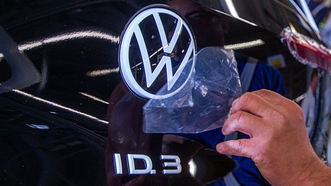 Ein Mitarbeiter entfernt eine Schutzfolie vom VW-Logo am Montageband für die Produktion des Elektroautos ID.3. © dpa - Bildfunk Foto: Jens Büttner