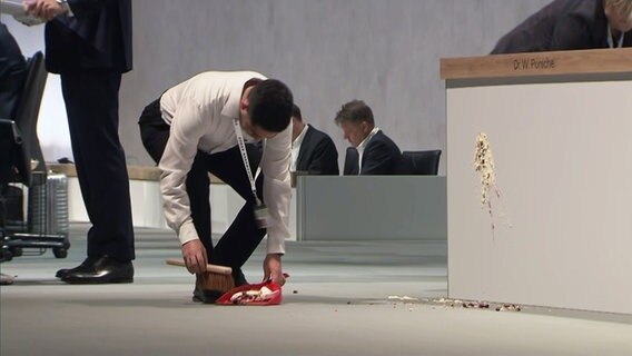 Ein Mann entfernt Tortenreste von der Bühne während der VW Hauptversammlung. © NDR 