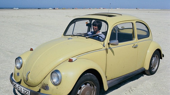 Eine Frau sitzt in einem alten VW Käfer am Strand an einem sonnigen Sommertag. ©  picture alliance / Moritz Vennemann 