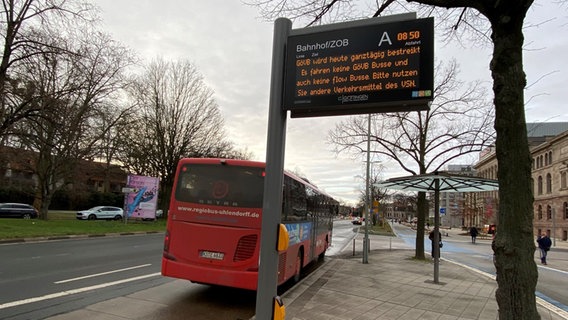Eine Anzeigetafel am ZOB Göttingen weist auf einen Warnstreik bei den Göttinger Verkehrsbetrieben hin, während ein Überlandbus der RBB dort hält. © NDR Foto: Bärbel Wiethoff