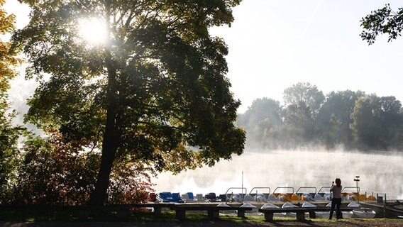 Eine Frau fotografiert den morgendlichen Nebel am Kiessee. ©  Swen Pförtner/dpa Foto:  Swen Pförtner/dpa